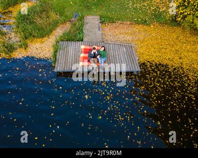 coppia posata sul molo al lago coperto di foglie autunnali Foto Stock