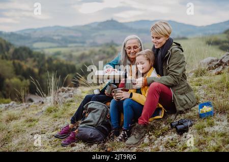 Bambina con madre e nonna seduta e bere tè caldo sulla cima della montagna in autunno. Foto Stock