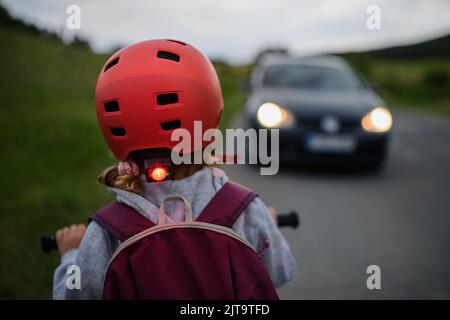 Vista posteriore del bambino in bicicletta su strada con auto di fronte a lei, concetto di educazione sulla sicurezza stradale. Foto Stock