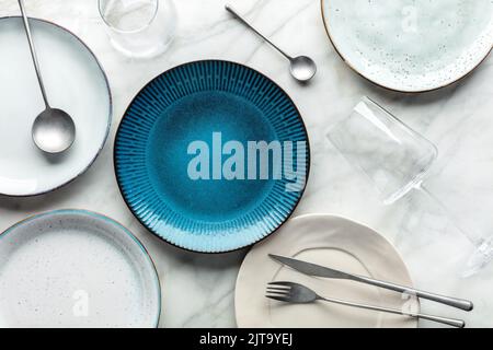 Set di stoviglie moderno con posate e un piatto blu vivace, con bicchieri, piatto a vista. Stoviglie alla moda su uno sfondo di marmo bianco Foto Stock