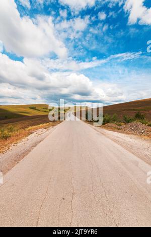 Strada asfaltata vuota attraverso la bella regione di Zlatibor paesaggio che si estende in prospettiva decrescente e scompare dietro la collina verde di questa fa Foto Stock