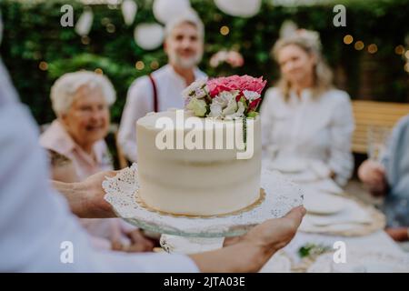 Sposa matura e sposo ottenere una torta al ricevimento di nozze all'esterno nel cortile. Foto Stock