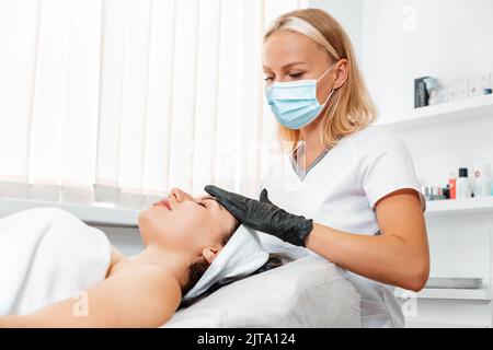 Un cosmetologo in una maschera medica massaggia un cliente in un salone di bellezza. Il concetto di ringiovanimento e trattamenti di bellezza. Foto Stock