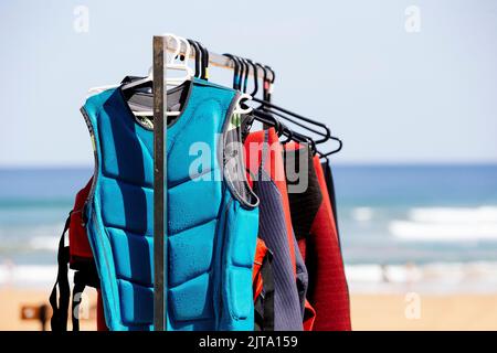 Una fila di mute appese su una rastrelliera in una scuola di surf Foto Stock