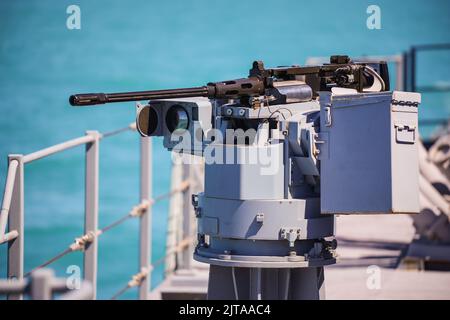 Immagine a colori di una mitragliatrice automatica sul ponte di una nave militare, in mare. Foto Stock