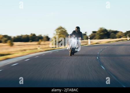 Un motociclista che corre lungo l'asfalto durante Gloden Hour Foto Stock