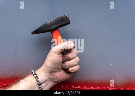 mano che tiene un martello con una maniglia corta in plastica su sfondo grigio Foto Stock