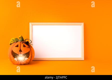 Concetto di festa di Halloween. Jack o lanterna con bokeh chiaro, decorazioni in carta fatte a mano, ragno e cornice bianca su sfondo arancione. Halloween Foto Stock
