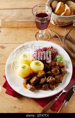 Dall'alto gulasch di manzo con gnocchi di patate e crauti serviti sul piatto vicino un bicchiere di vino rosso e ciotola di vimini con pane fresco su tavola di legname i Foto Stock