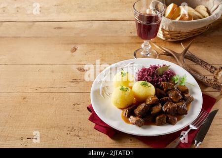 Dall'alto gulasch di manzo e gnocchi di patate con crauti serviti sul piatto vicino al vino rosso e pane su tavola di legno con corna di cervo e cutle Foto Stock