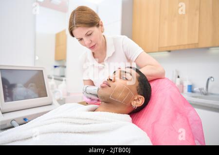 Clinica di bellezza medico donna che esegue la procedura di lifting con dispositivo a ultrasuoni Foto Stock