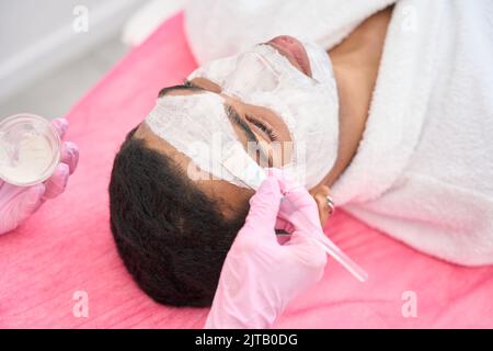 Estetista applicare maschera a faccia di cliente maschile con pennello Foto Stock