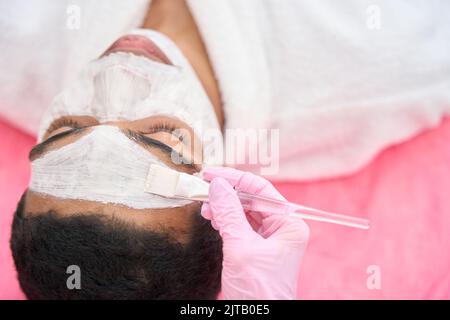 Estetista che applica la maschera alla pelle del giovane uomo Foto Stock