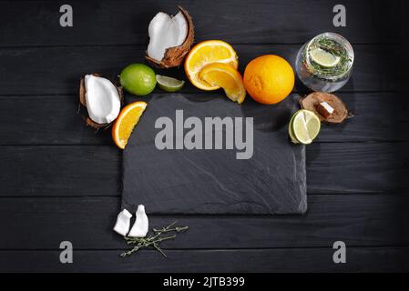 abboiate l'ardesia con frutta tropicale. Mockup set di frutta tropicale lime, cocco su, arancione, lo sfondo di un vecchio tavolo di legno scuro, vista dall'alto, appartamento Foto Stock