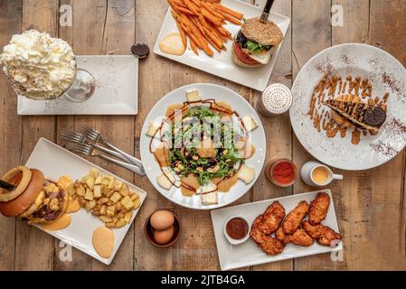 Set di fast food con insalate e pezzo di torta, hamburger con patatine fritte, insalata con formaggio e cotogna, pollo più piccante Foto Stock