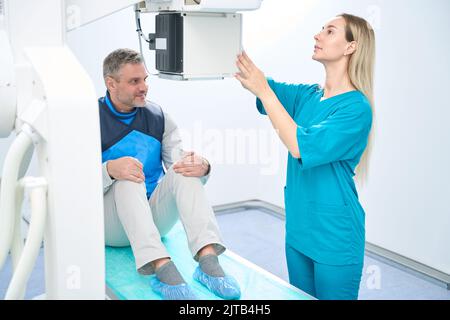 Il paziente sorridente attende che il medico completi la regolazione della macchina a raggi X. Foto Stock