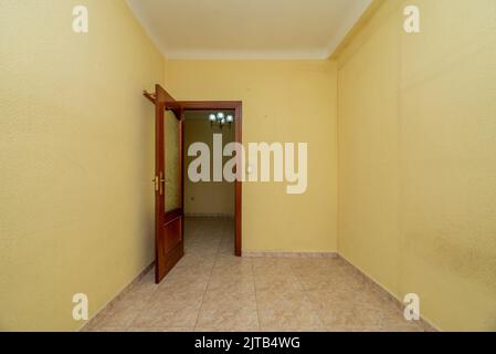 La piccola camera vuota è con pavimento in gres di piastrelle quadrate, parete dipinta di giallo con gotelet e porta di legno rossiccio con finestra di vetro Foto Stock