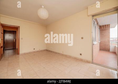 la stanza vuota ha pavimento in gres di mattonelle quadrate, parete dipinta di crema con gotelet, accesso ad una terrazza con pavimenti di argilla e porta di legno rossiccio con vetro w. Foto Stock