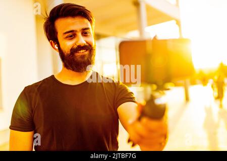 uomo bearded in cotone nero t-shirt registrazione video per vegan blog all'aperto nel parco estivo al tramonto luce oro Foto Stock