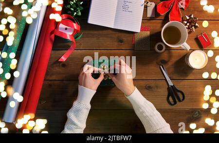 mani che imballano il regalo di natale e che attaccano l'arco Foto Stock