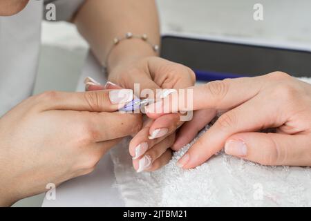 dettaglio delle mani di un manicure latino che esegue la corretta pulizia delle unghie con un paio di pinze o forbici da cuticola, rimuovendo il de Foto Stock