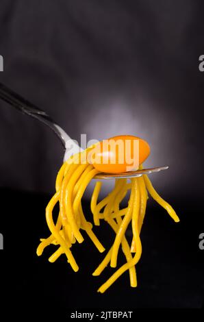 Macro immagine di Mini pomodoro Ciliegio giallo con spaghetti curcuma su forchetta verticale Foto Stock