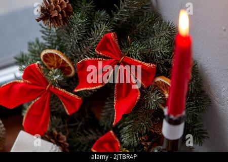 corona di natale con archi rossi e candela accesa Foto Stock