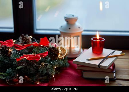 corona di natale, libri, candela, lanterna sulla finestra Foto Stock