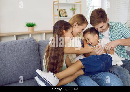 Famiglia allegra con bambini che si divertono insieme e che si divertono a fare il solletico sul divano del soggiorno Foto Stock