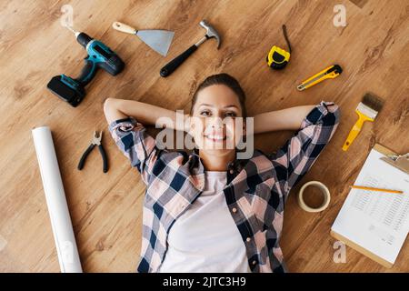 donna con attrezzi da lavoro sdraiata su pavimento in legno Foto Stock