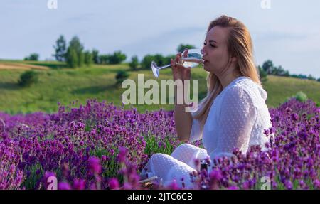 una ragazza in un campo di lavanda versa il vino in un bicchiere. Rilassamento. Fuoco selettivo Foto Stock