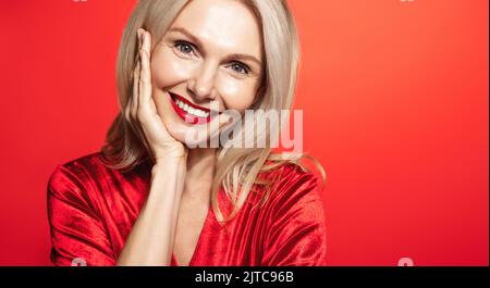 Ritratto di donna anziana romantica, donna elegante in abito rosso e rossetto rosso, guardando con anelito da parte a copiare spazio, concetto di vacanze invernali Foto Stock