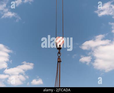 Il gancio della gru con strisce rosse e bianche pensili, cielo blu in background. Foto Stock