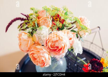Bouquet fresco di rose zinnia fiori amaranto messo in vaso su tavola. Processo di sistemazione con cestino e potatrice Foto Stock