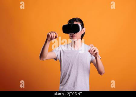 Uomo in occhiali vr che gioca a videogame di realtà virtuale, esplorando il metaverse. Adolescente in piedi indossa un casco, goditi l'esperienza di simulazione, l'intrattenimento nel cyberspazio, lo stile di vita moderno Foto Stock