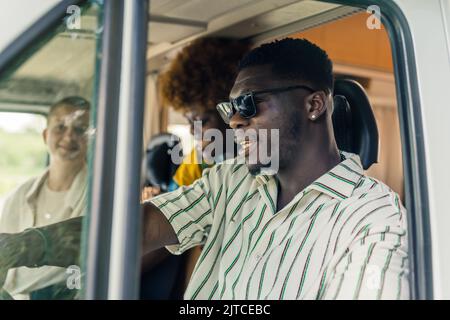Uomo afro-americano con i suoi amici alla guida di un furgone, closeup medio all'aperto concetto di viaggio. Foto di alta qualità Foto Stock