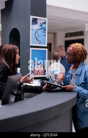 Donna addetta al ricevimento, donna che aiuta alla reception, firmando documenti medici per ricevere assistenza assicurativa prima dell'appuntamento di controllo. Il paziente compila il modulo di registrazione per eseguire l'esame. Foto Stock