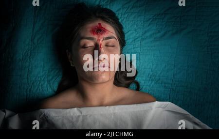 Ghost giovane donna con una ferita sanguinosa sulla fronte con gli occhi chiusi su una barella coperta da un foglio. Halloween e concetto di orrore Foto Stock