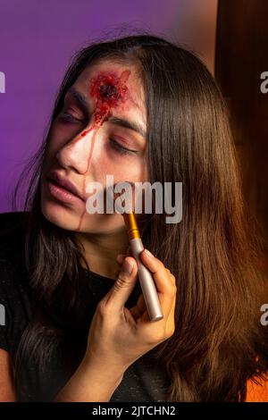 Primo piano di una giovane donna che mette sul trucco di Halloween con un'immagine di zombie con una ferita sulla sua fronte Foto Stock