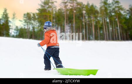 Little Boy con slitta salendo la collina di neve in inverno Foto Stock