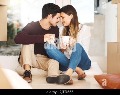 Una giovane coppia affettuosa che prende una pausa caffè mentre si sposta in una nuova casa. Foto Stock