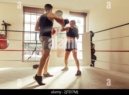 Allenatore maschile che aiuta giovani pugile femminile con tecniche sorprendenti in un anello di pugilato. Giovane allenatore di pugilato allenando una giovane donna in palestra. Foto Stock