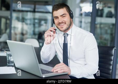 Qui per offrire assistenza. Ritratto di un giovane rappresentante del servizio clienti che indossa una cuffia mentre è seduto alla sua postazione di lavoro in ufficio. Foto Stock