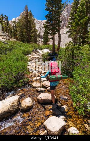 Escursionista che attraversa Lone Pine Creek sul Mount Whitney Trail, John Muir Wilderness, California USA Foto Stock