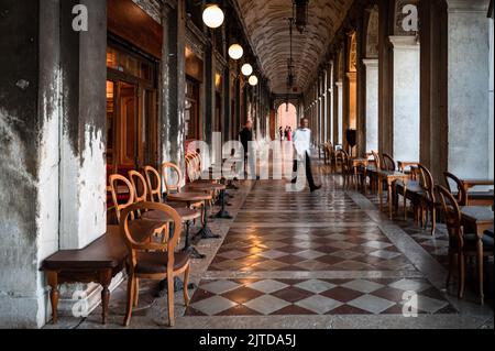 Venezia, Italia. 21st ago, 2022. Un dipendente del CafÃˆ Florian attraversa il vicolo colonnato lungo Piazza San Marco. Inizialmente annunciata per giugno 2022, la tassa di ingresso per i viaggiatori di un giorno a Venezia sarà applicata solo a partire dal 16° gennaio 2023. Stordito dalla pandemia del 19 nel 2021, dalla fine delle restrizioni sanitarie in Italia nel 2022 fino a 110.000 giorni di turisti visitano la città, mentre la popolazione permanente della città è stimata in circa 50.000 persone. L'introduzione di tasse e restrizioni per i visitatori sui siti naturali e culturali più frequentati, noto come la lotta contro il sovra-turismo, è Foto Stock