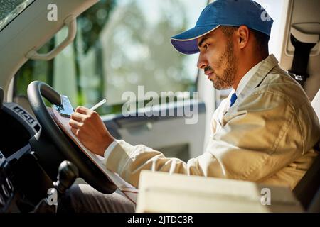 Mantenere i tempi di consegna richiede un po' di concentrazione: Un addetto alla consegna che scrive su un clipboard mentre si siede nel suo furgone. Foto Stock