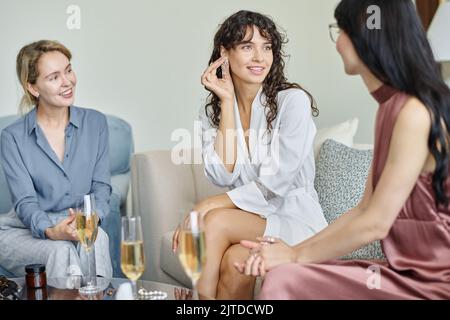 Felice giovane sposa di provare su nuovi orecchini mentre due amici aiutandola a scegliere gli accessori adatti durante la preparazione per il matrimonio Foto Stock