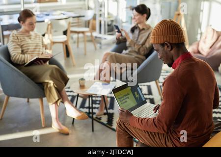 Vista laterale ritratto di giovane uomo nero a scrivere al computer portatile con le statistiche di marketing sullo schermo in ufficio aziendale, copia spazio Foto Stock