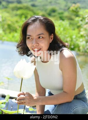 Giovane donna vietnamita sorridente e odora un loto bianco in Vietnam Foto Stock