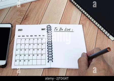 Mani con la penna che scrive per fare l'elenco con il calendario di maggio 2023 sul notebook. Foto Stock